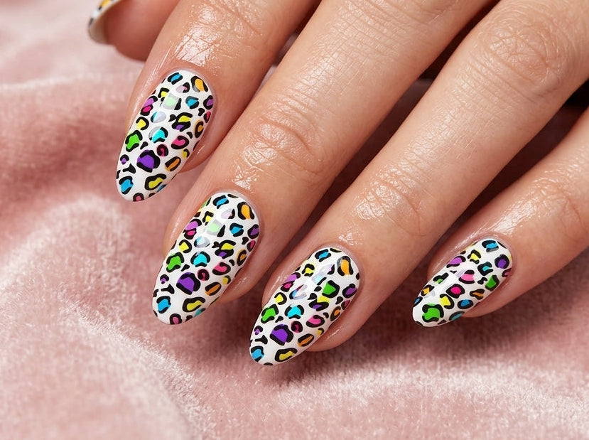 Hand with colorful leopard print nail design on a pink fabric background