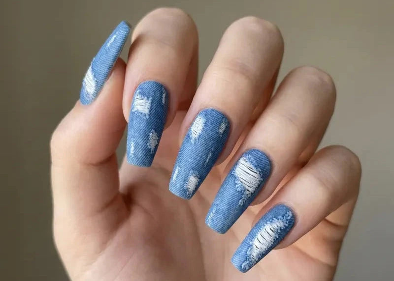 Hand with blue distressed nail art on a neutral background