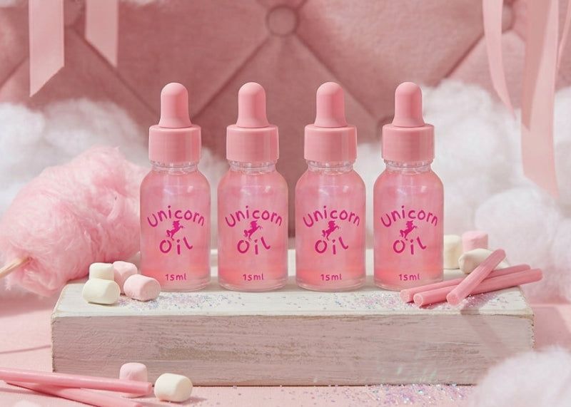 Pink bottles labeled 'Unicorn Oil' on a pink cushioned background with cotton candy.