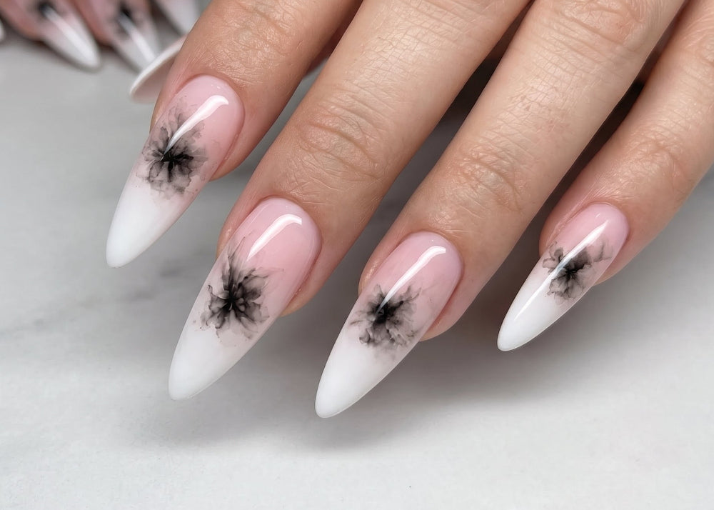 Close-up of hands with pink and white nail polish featuring black abstract designs on a marble surface.