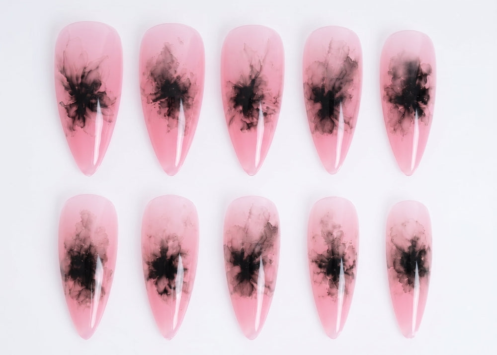 Pink nail art with black abstract designs on a white background
