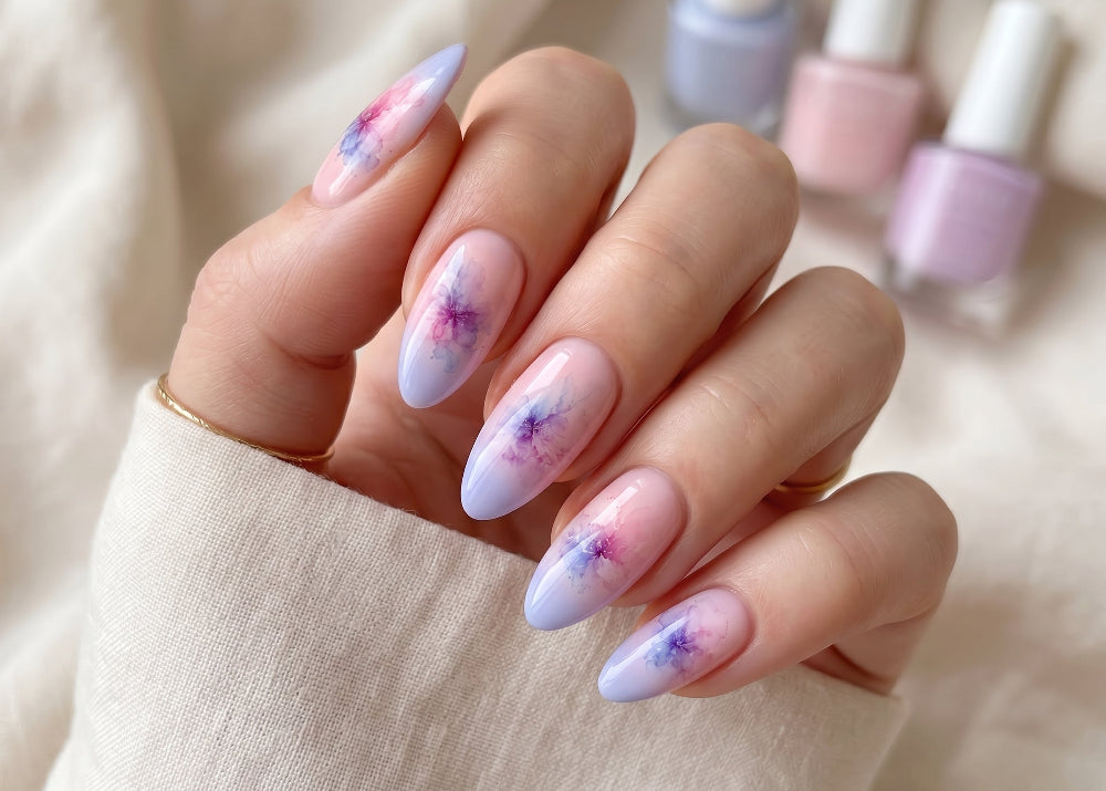 Hand with pastel gradient nails featuring floral designs, with nail polish bottles in the background.