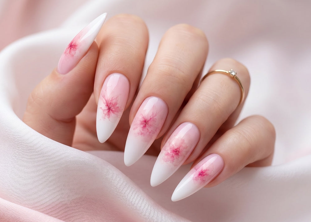 Hand with almond-shaped nails featuring pink floral designs on a soft pink fabric background