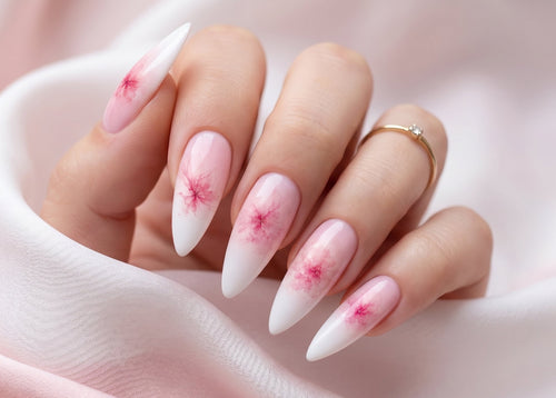 Hand with almond-shaped nails featuring pink floral designs on a soft pink fabric background