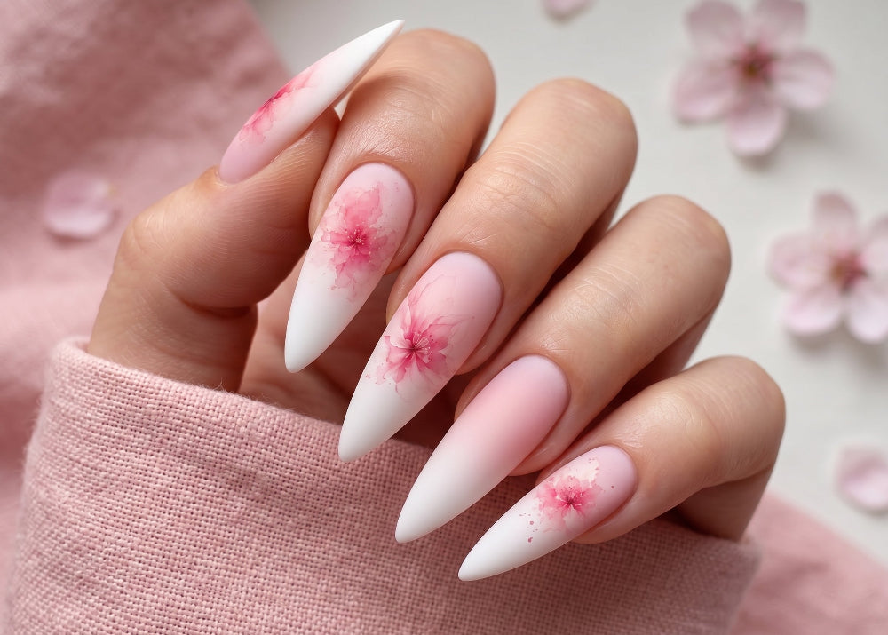 Hand with almond-shaped nails featuring pink flower designs on a soft pink background.