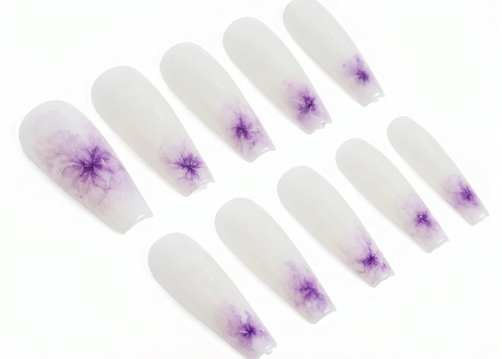 Set of white press-on nails with purple flower designs on a white background