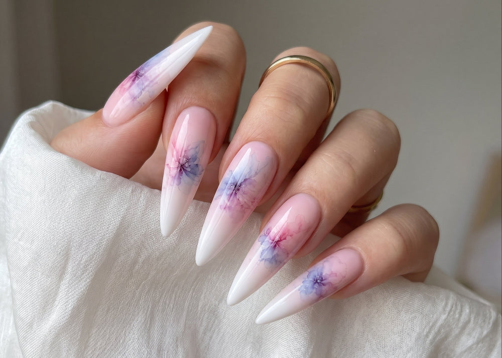 Hand with long, pointed nails featuring a floral design on a neutral background