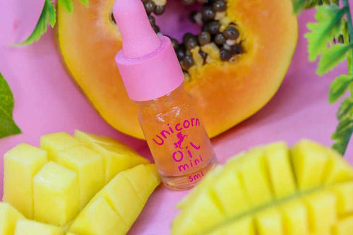 Mango & Guava Unicorn Cuticle Oil 5ml mini sized nail serum in dropper bottle with pink cap. Bottle is standing near a cut mango and guava fruit.